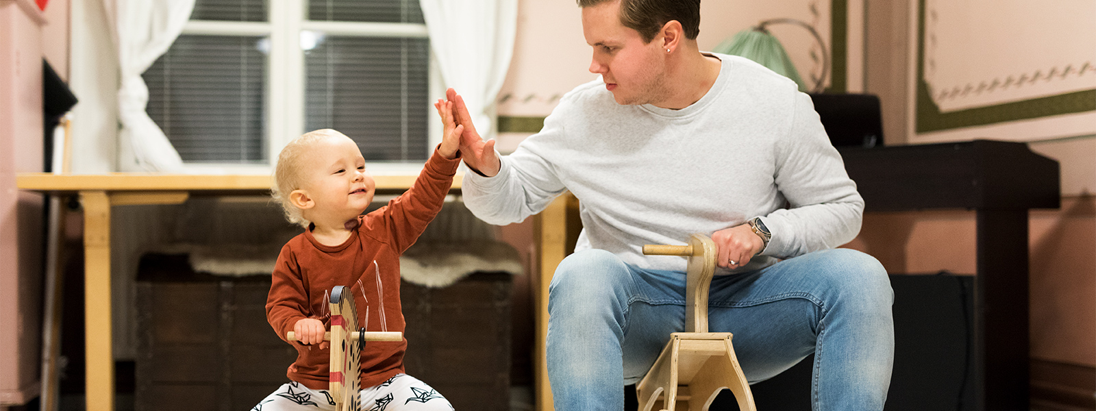 Isä ja lapsi istuvat keinuhevosilla